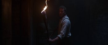 Movie still from “The Nun” (2018), directed by Corin Hardy – A man is holding a burning torch in the dark; Medium shot, Low angle