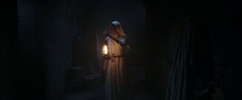 Movie still from “The Nun” (2018), directed by Corin Hardy – A nun holding a lantern in a dark room; Wide shot, Low angle