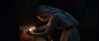Movie still from “The Nun” (2018), directed by Corin Hardy – A woman is lighting a candle in the dark; Medium shot, Low angle