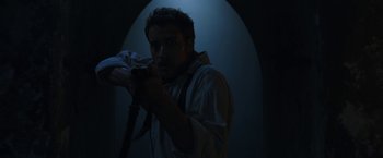 Movie still from “The Nun” (2018), directed by Corin Hardy – A man holding a rifle in a dark room; Medium shot, Low angle