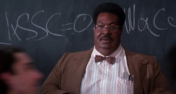 Movie still from “The Nutty Professor” (1996), directed by Tom Shadyac – A man wearing a suit and bow tie in front of a chalkboard; Medium shot, Over the shoulder angle