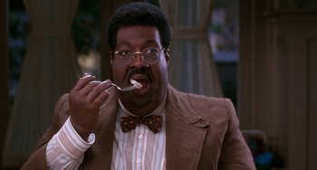 Movie still from “The Nutty Professor” (1996), directed by Tom Shadyac – A man in a suit and bow tie eating a spoon; Medium shot, High angle