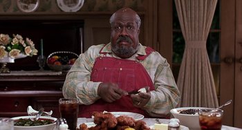 Movie still from “The Nutty Professor” (1996), directed by Tom Shadyac – A man sitting at a dinner table holding a knife; Medium shot, Low angle