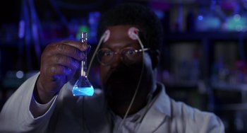 Movie still from “The Nutty Professor” (1996), directed by Tom Shadyac – A man in a lab coat holding up a blue liquid; Close Up shot, High angle
