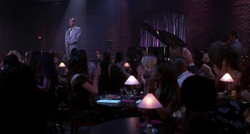 Movie still from “The Nutty Professor” (1996), directed by Tom Shadyac – A group of people sitting at tables in front of a man singing; Wide shot, High angle