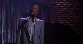Movie still from “The Nutty Professor” (1996), directed by Tom Shadyac – A man in a blue suit is singing into a microphone; Medium shot, High angle