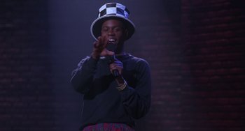Movie still from “The Nutty Professor” (1996), directed by Tom Shadyac – A man wearing a hat is singing into a microphone; Medium shot, Low angle