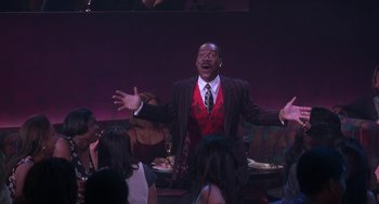 Movie still from “The Nutty Professor” (1996), directed by Tom Shadyac – A man wearing a suit and tie standing in front of a group of people; Medium shot, Low angle