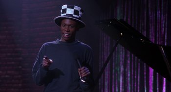 Movie still from “The Nutty Professor” (1996), directed by Tom Shadyac – A man wearing a black and white hat and holding a microphone; Medium shot, High angle