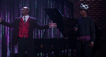 Movie still from “The Nutty Professor” (1996), directed by Tom Shadyac – A man in a suit and tie holding a piano; Medium shot, Over the shoulder angle