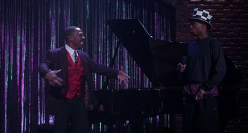 Movie still from “The Nutty Professor” (1996), directed by Tom Shadyac – A man standing next to a piano in front of a purple curtain; Medium shot, High angle