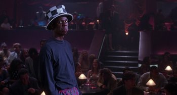Movie still from “The Nutty Professor” (1996), directed by Tom Shadyac – A man wearing a hat standing in front of a group of people; Medium shot, Over the shoulder angle