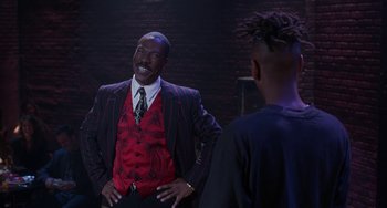 Movie still from “The Nutty Professor” (1996), directed by Tom Shadyac – A man standing next to another man in a suit; Medium shot, Over the shoulder angle
