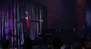 Movie still from “The Nutty Professor” (1996), directed by Tom Shadyac – A man standing on a stage in front of an audience; Extreme Wide shot, High angle