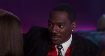 Movie still from “The Nutty Professor” (1996), directed by Tom Shadyac – A man in a suit and tie sitting in front of a purple background; Close Up shot, Low angle