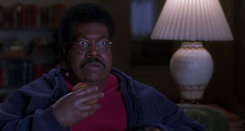 Movie still from “The Nutty Professor” (1996), directed by Tom Shadyac – An older man sitting at a table eating a donut; Close Up shot, High angle