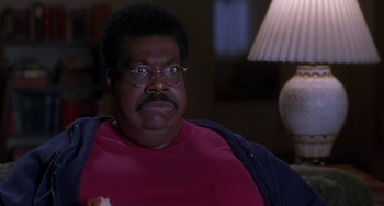 Movie still from “The Nutty Professor” (1996), directed by Tom Shadyac – A person sitting in a chair wearing glasses; Close Up shot, High angle