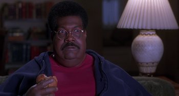 Movie still from “The Nutty Professor” (1996), directed by Tom Shadyac – A man sitting in a chair holding a donut; Close Up shot, High angle