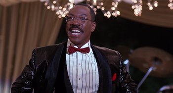 Movie still from “The Nutty Professor” (1996), directed by Tom Shadyac – A man in a suit and bow tie smiling; Close Up shot, Low angle
