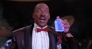 Movie still from “The Nutty Professor” (1996), directed by Tom Shadyac – A man in a suit holding up a bottle of liquid; Close Up shot, High angle