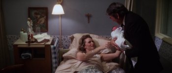 Movie still from “The Omen” (1976), directed by Richard Donner – A woman and a man holding a baby in a hospital bed; Medium shot, High angle
