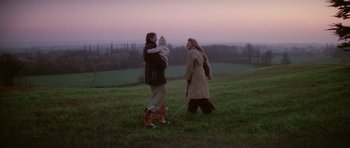 Movie still from “The Omen” (1976), directed by Richard Donner – A man and a woman walking a dog on a field; Wide shot, High angle
