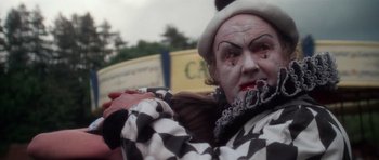 Movie still from “The Omen” (1976), directed by Richard Donner – A man dressed up as a harlequin for a parade; Close Up shot, Over the shoulder angle