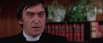 Movie still from “The Omen” (1976), directed by Richard Donner – A man in a priest's outfit stares into the camera; Close Up shot, Low angle