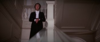 Movie still from “The Omen” (1976), directed by Richard Donner – A woman standing in front of a table in a room; Medium shot, Low angle