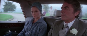 Movie still from “The Omen” (1976), directed by Richard Donner – A woman sitting in the back of a car next to a man; Medium shot, Over the shoulder angle