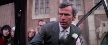Movie still from “The Omen” (1976), directed by Richard Donner – An older man wearing a suit and a white flower; Close Up shot, Over the shoulder angle