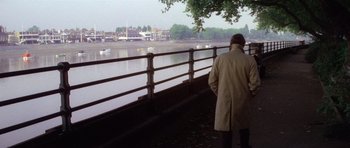 Movie still from “The Omen” (1976), directed by Richard Donner – A man in a trench coat looking out over a river; Extreme Wide shot, High angle