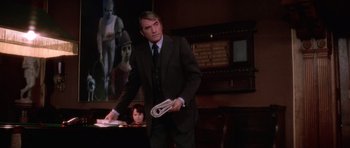 Movie still from “The Omen” (1976), directed by Richard Donner – A man in a suit and tie holding a newspaper; Medium shot, Low angle
