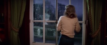 Movie still from “The Omen” (1976), directed by Richard Donner – A woman looking out of a window at a rainy night; Medium shot, High angle