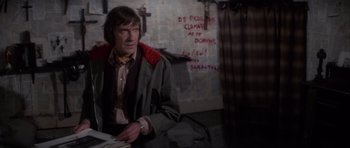 Movie still from “The Omen” (1976), directed by Richard Donner – A man sitting at a table in front of a wall; Medium shot, Over the shoulder angle