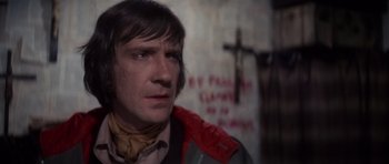 Movie still from “The Omen” (1976), directed by Richard Donner – A man in a red and gray jacket looking to his left; Close Up shot, Over the shoulder angle