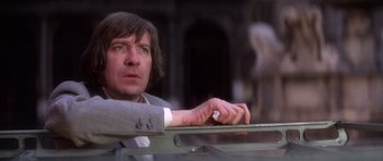 Movie still from “The Omen” (1976), directed by Richard Donner – A man leaning on a railing looking at the camera; Close Up shot, Low angle