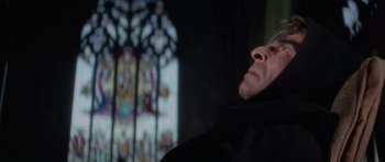 Movie still from “The Omen” (1976), directed by Richard Donner – A man in a black robe looking up at a stained - glass window; Close Up shot, Low angle