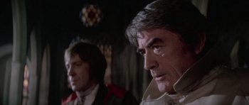 Movie still from “The Omen” (1976), directed by Richard Donner – Two men in a room with a stained - glass window in the background; Close Up shot, Over the shoulder angle