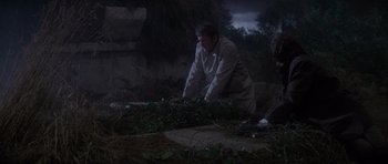 Movie still from “The Omen” (1976), directed by Richard Donner – A man kneeling down in the grass at night; Wide shot, High angle