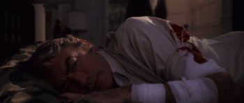 Movie still from “The Omen” (1976), directed by Richard Donner – A man laying on the ground with a bandage on his arm; Close Up shot, High angle