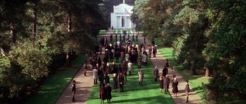 Movie still from “The Omen” (1976), directed by Richard Donner – A crowd of people walking down a path in front of a white building; Extreme Wide shot, High angle