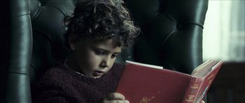 Movie still from “The Orphanage” (2007), directed by J.A. Bayona – A young boy is reading a red book; Close Up shot, High angle