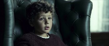 Movie still from “The Orphanage” (2007), directed by J.A. Bayona – A young boy sitting in a chair looking into the distance; Close Up shot, High angle
