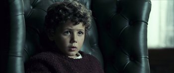Movie still from “The Orphanage” (2007), directed by J.A. Bayona – A young boy sitting in a chair looking at the camera; Close Up shot, High angle