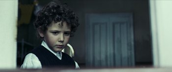 Movie still from “The Orphanage” (2007), directed by J.A. Bayona – A young boy with curly black hair wearing a vest; Close Up shot, Over the shoulder angle