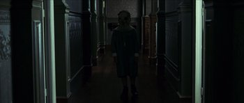 Movie still from “The Orphanage” (2007), directed by J.A. Bayona – A person with a mask standing in a dark room; Medium shot, Low angle