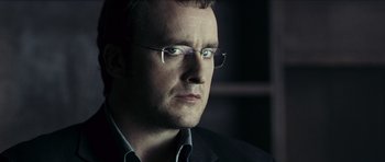 Movie still from “The Orphanage” (2007), directed by J.A. Bayona – A person wearing glasses and a suit; Close Up shot, Low angle