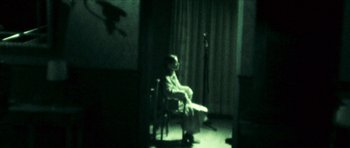 Movie still from “The Orphanage” (2007), directed by J.A. Bayona – A man sitting in a chair in front of a microphone in a dark room; Wide shot, High angle