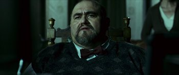 Movie still from “The Orphanage” (2007), directed by J.A. Bayona – A man sitting in a chair wearing a bow tie; Close Up shot, Low angle